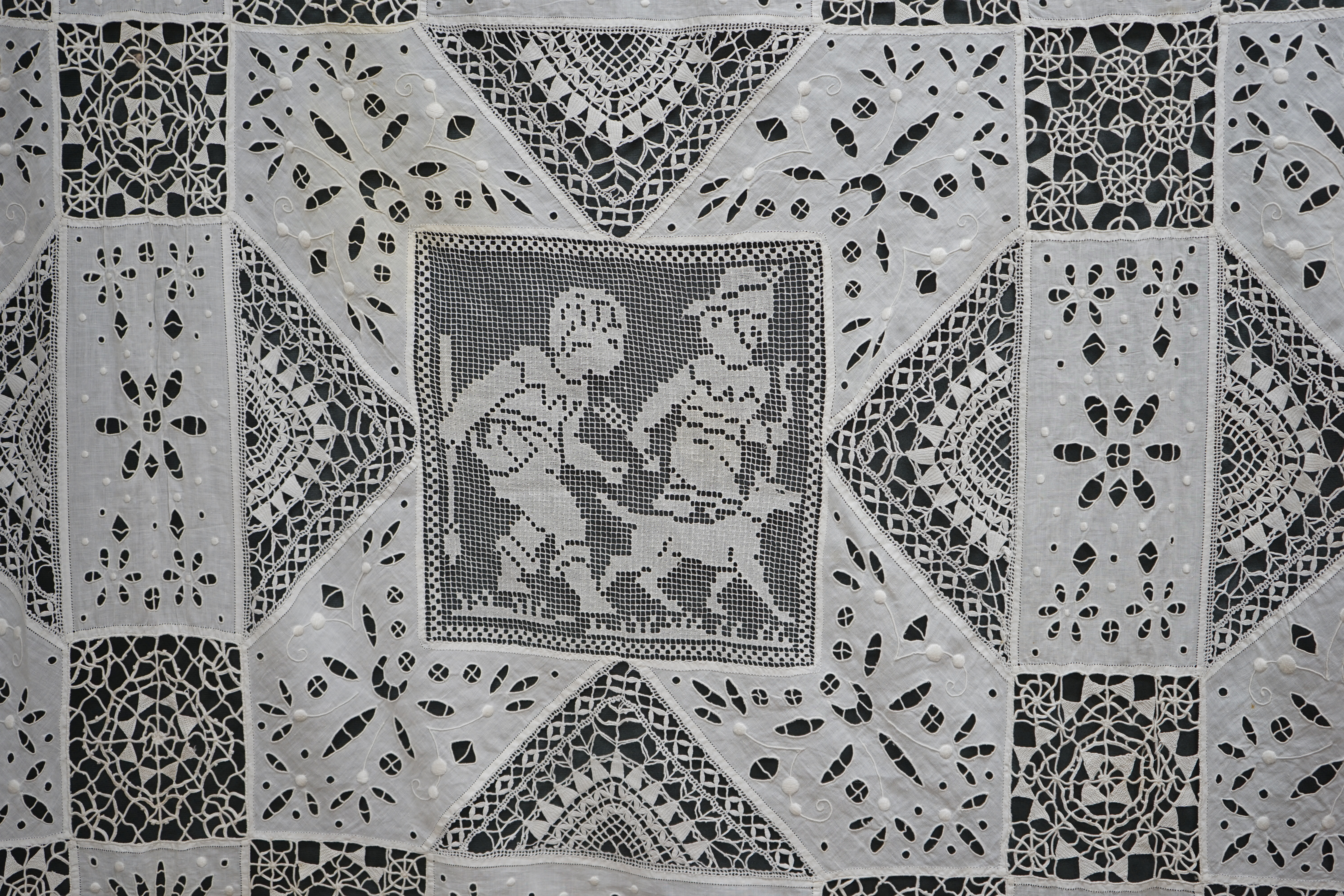 An early 20th century Italian ornate bedcover, worked with square fillet lace insertions of putti, white multi patterned cut work squares on fine linen and similar multi patterned needle lace squares, creating a unique b